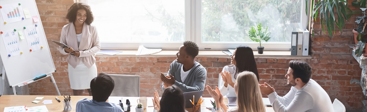 woman doing a presentation at a meeting receiving applaud from a group of peers